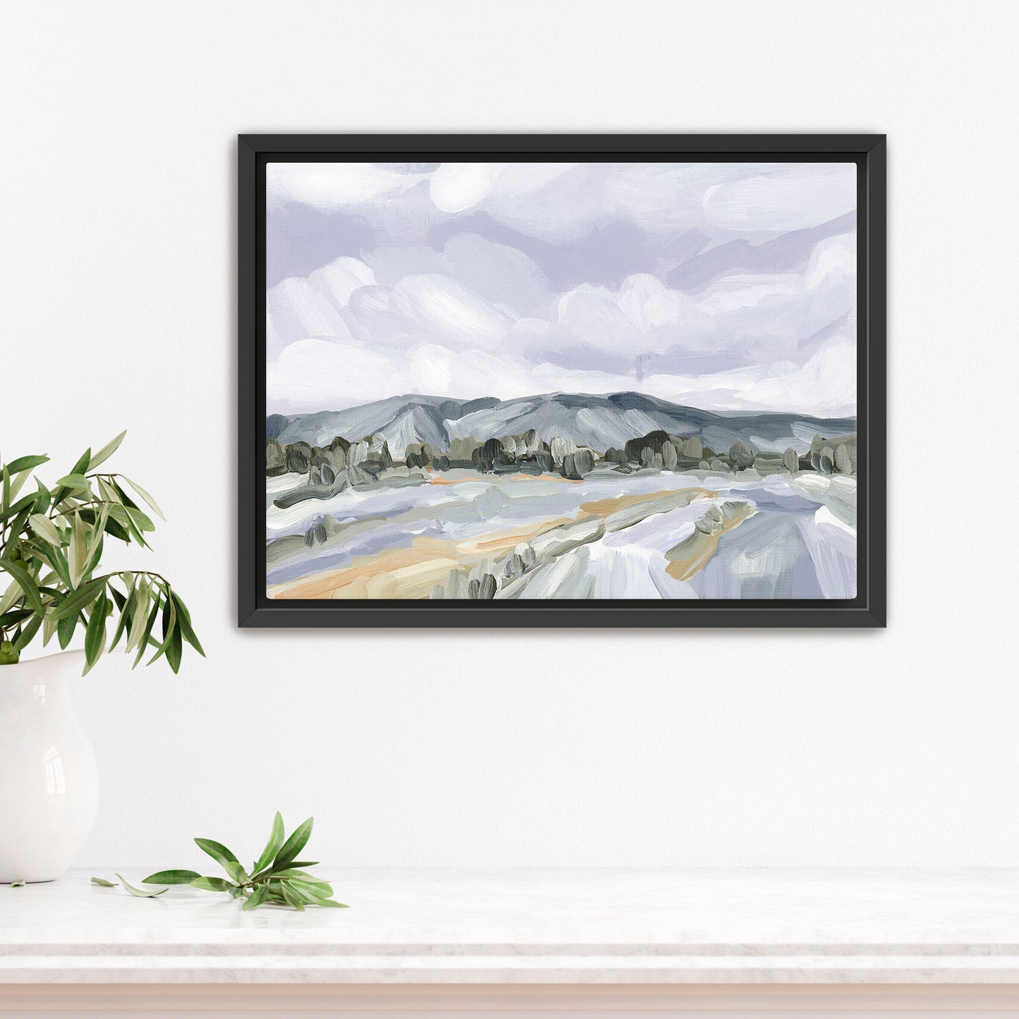 Framed landscape painting depicting mountains, fields, and cloudy sky in muted colors.