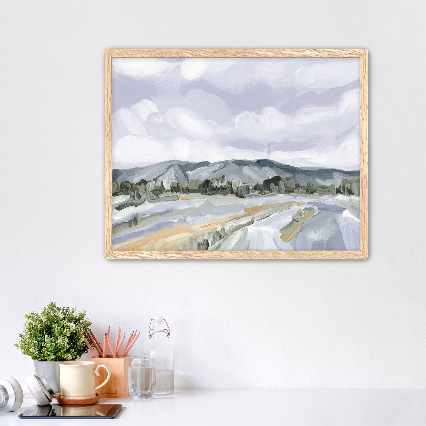 Framed landscape painting depicting mountains and fields under a cloudy sky.