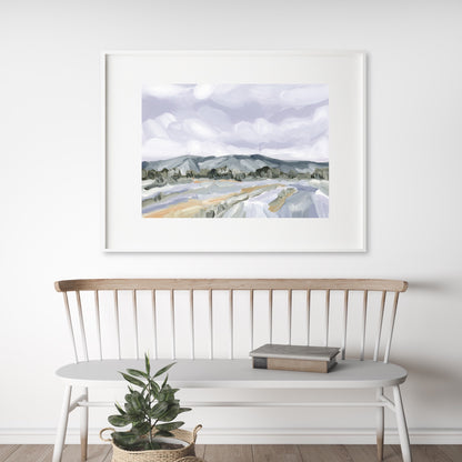 Framed watercolor landscape painting of mountains and fields hanging above a white wooden bench.