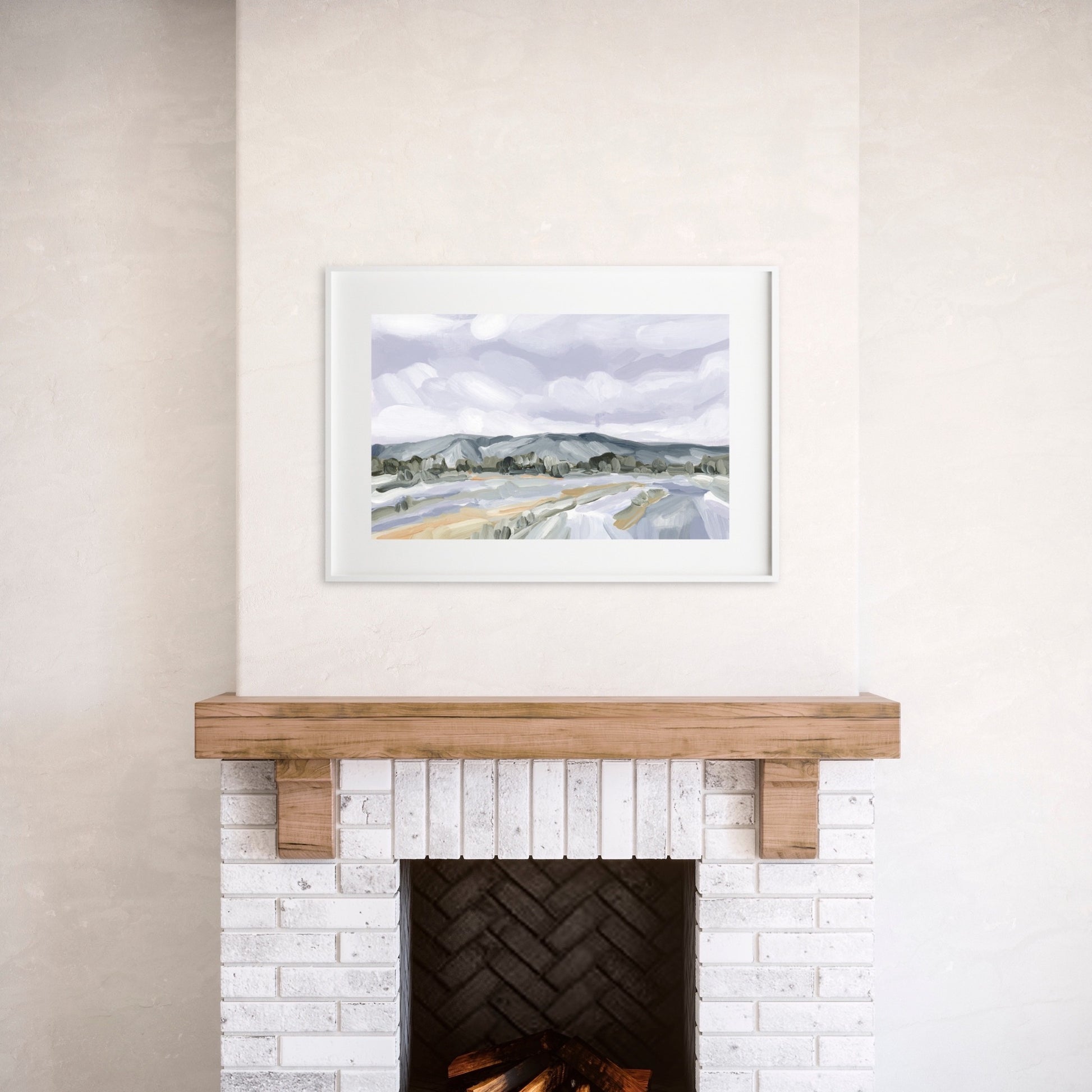 Framed landscape painting hanging above a fireplace with a wooden mantel.