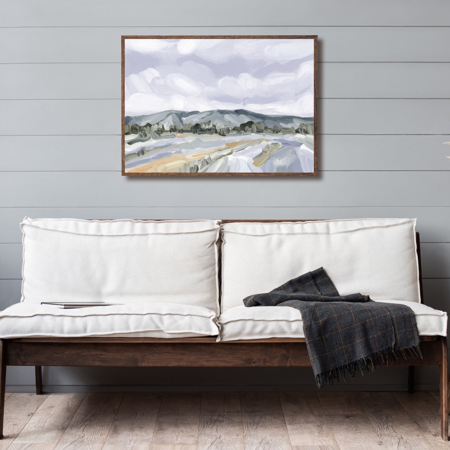 White sofa with wooden frame and a dark throw blanket draped over one end.