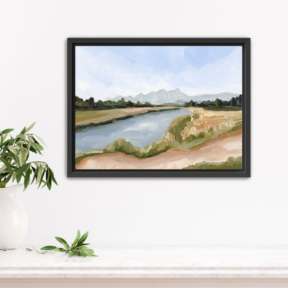 Framed landscape painting depicting a river, grassy banks, and distant mountains.