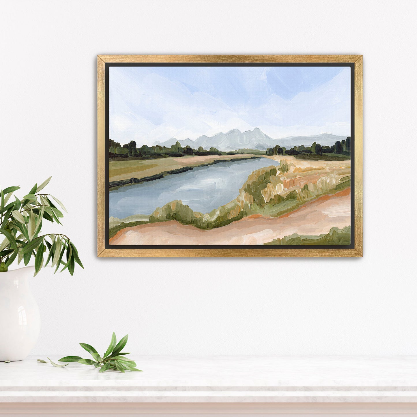 Framed landscape painting depicting a river, grassy banks, and distant mountains.