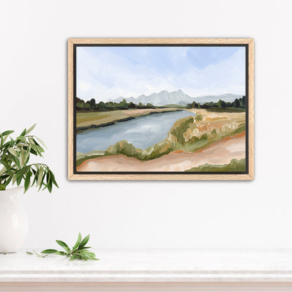 Framed landscape painting depicting a river, grassy banks, and distant mountains.