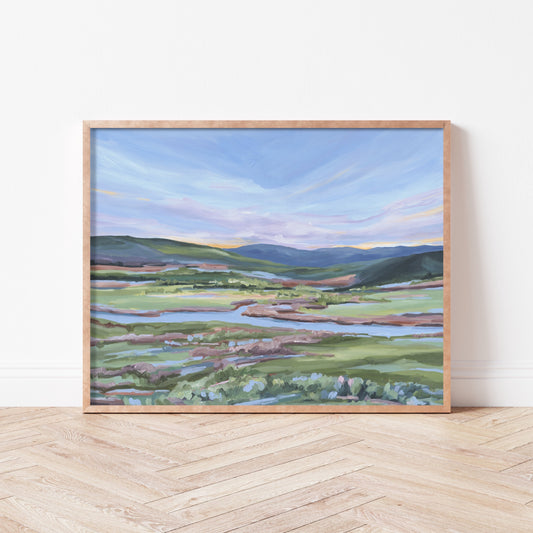 Framed landscape painting depicting rolling hills, fields, and a winding river.