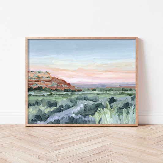 Framed landscape painting depicting a desert scene with mountains and scrub vegetation.