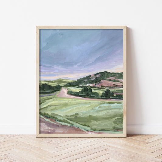 Framed landscape painting depicting rolling green hills and a winding path under a cloudy sky.