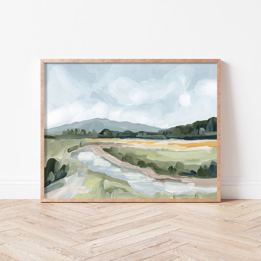 Framed landscape painting depicting a rural countryside with fields and distant hills.